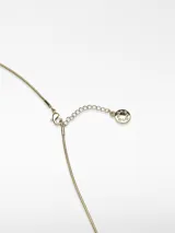 Collar largo de cadena fina dorada con un dije metálico de forma orgánica y relieve irregular, que incluye un aplique de perla natural en el centro. Cuenta con cierre de mosquetón y cadena de alargue con terminal logotipado.