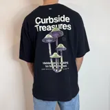 Remera negra de corte oversize con estampa en la espalda que incluye texto "Curbside Treasures" y un grupo de hongos.