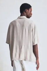 Camisa de manga corta color beige con cuello abierto, tapeta lisa, bolsillo superior y bajo recto. Corte estándar para una silueta clásica y cómoda.