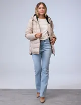 Campera acolchada tipo puffer de color beige, con costuras horizontales y capucha integrada con cordones ajustables negros. Presenta cierre frontal negro y bolsillos laterales.
