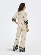 Pantalón de pierna ancha color crema con estampado de hojas negras, cintura elástica trasera y bolsillos frontales.