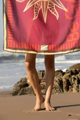 Pareo rectangular fucsia con estampado de sol dorado y borde con diseño geométrico en tonos naranja y marrón.