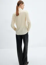 Camisa color crema de corte recto, con cuello camisero, cierre frontal con botones y mangas largas con puños abotonados.