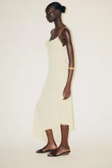 Vestido midi color crema confeccionado en encaje, con escote recto, tirantes finos, volantes y tachas.