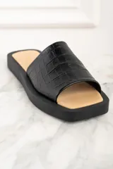 Sandalia abierta negra con textura de cuero de cocodrilo y suela plana.