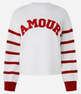 Suéter blanco de jacquard con letras 'Amour' en rojo y rayas horizontales rojas en las mangas.