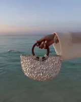 Bolso de mano con forma de media luna cubierto de perlas sintéticas. Tiene asas circulares de madera y detalles de cuentas en la unión con el cuerpo del bolso.