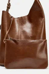 Bolso marrón de cuero, formato saca asimétrica. Tiene asa de hombro ajustable y cierre con imán. Incluye una cartera con bolsillo extraíble.
