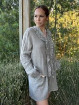 Camisa blanca de lino con cuello mao, mangas largas abullonadas y cierre frontal con botones de nácar. Presenta volados en el frente y puños elásticos.