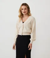 Cardigan corto de punto color crema, con escote en V, abotonadura frontal y mangas largas abullonadas con puños acanalados. Presenta un punto calado en forma de rombos en la parte superior del busto y en las mangas.
