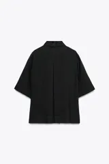 Camisa negra de manga corta confeccionada en hilatura con lyocell y ramio, con cuello solapa, bajo recto y cierre frontal con botones.