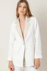 Blazer de lino color blanco con solapas y cuello en color beige, corte entallado, botón de nácar, tajo en la espalda y bolsillos laterales.