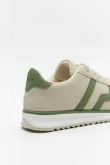 Zapatillas beige con recortes en gamuza de diferentes tonos, cordones y suela irregular blanca con detalle rosa.