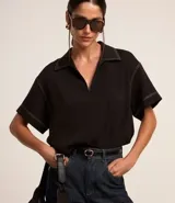 Blusa negra de manga corta con cuello camisero y escote en V. Presenta pespuntes blancos contrastantes en cuello, mangas y hombros.