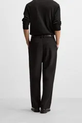 Pantalón negro de corte amplio, con pliegues en la parte delantera, bolsillos laterales y traseros de ojal.
