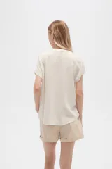 Blusa color crudo de viscosa, corte holgado, con cuello en v y cierre frontal con dos botones de madera.