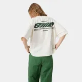 Camiseta color arena de corte cuadrado con cuello polo y estampado en la espalda con el logo de la marca Eme Studios y la frase "Building a community through gratitude".