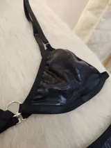 Conjunto de bikini negro de cuerina texturizada, con corpiño triangular con aro metálico central y bombacha colaless con tiras laterales ajustables.