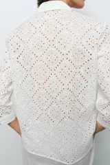 Camisa amarilla de cuello solapa y manga larga acabada en puño. Detalle de bordados perforados a tono. Cierre frontal con botones ocultos por solapa.