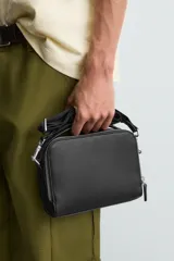 Bandolera negra con textura grabada, compartimento principal con cierre de cremallera, bolsillo interior con cremallera, bolsillo trasero con cremallera y asa de hombro ajustable.