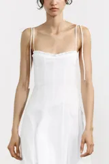 Vestido midi blanco de popelín con escote corazón y volantes. Tiene tirantes finos con detalle de lazo, forro interior combinado y cierre lateral con cremallera oculta.