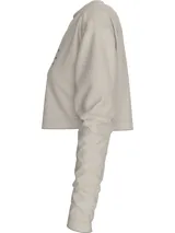 Remera cropped color beige de algodón, con cuello redondo y mangas largas. Presenta el logo de Calvin Klein Jeans estampado en el pecho.