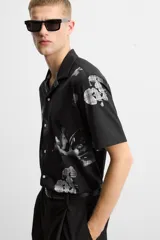 Camisa negra con estampado floral en tonos grises, de manga corta y cuello bowling.