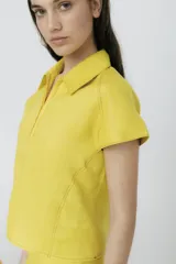 Blusa amarilla de lino con cuello polo, mangas cortas y cierre frontal con cremallera.