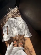 Blusa blanca de encaje con cuello en V, mangas largas acampanadas y lazo ajustable en el frente.