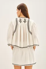 Camisa blanca de algodón con bordado negro en el ruedo, corte amplio y largo corto. Escote redondo y mangas largas abullonadas.