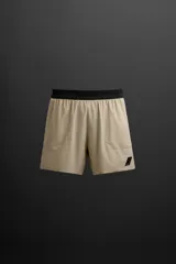 Shorts deportivos color beige con cintura elástica negra, bolsillos laterales y logo estampado en la pierna.