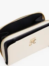 Billetera Tommy Hilfiger color crema con cierre de cremallera y botón a presión. Cuenta con compartimento interior para billetes y múltiples ranuras interiores para tarjetas. Luce el monograma TH metálico en la parte delantera.