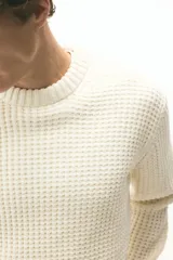 Buzo de punto texturizado suave de chenille, color crema, con cuello redondo ribeteado, hombros caídos y puños y bajo en punto acanalado.