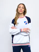 Buzo de felpa azul marino con mangas raglán rojas y detalles tricolor en puños, mangas y cuello. Incluye logo de Umbro bordado en el pecho y escudo del Club Nacional de Football.
