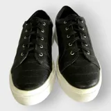 Zapatillas urbanas negras con textura de cocodrilo, cordones negros y suela de goma blanca.