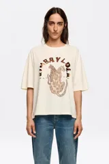 Remera color crema de corte recto, cuello redondo y manga corta. Estampado frontal con dos leopardos y el logo de la marca en marrón.