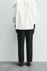 Pantalón chino negro de corte relajado (relaxed fit) con tiro medio, confeccionado en algodón con elasticidad. Presenta bolsillos delanteros y bolsillos traseros de vivo, con cierre frontal de cremallera y botón.