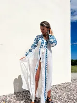 Túnica playera blanca traslúcida con bordados azules, mangas largas y abertura frontal.