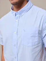 Camisa de algodón blanca de manga corta, con cuello abotonado y botones frontales.