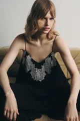 Vestido midi negro de tejido plisado, con escote pico, tirantes finos ajustables y aplicación de encaje y bordados florales combinados a contraste.