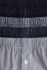 Pack de cinco calzoncillos boxer de algodón con cintura elástica, piernas largas y cierre de botón. Incluye calzoncillos lisos en azul marino, a rayas verticales en azul y blanco, y a cuadros en azul y blanco.