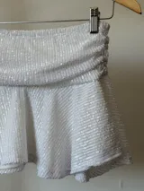 Minifalda blanca con lentejuelas, cintura alta fruncida y corte acampanado.