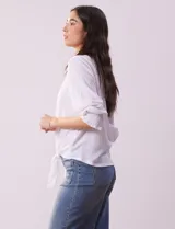 Blusa blanca de tejido texturado con cuello redondo, escote en V con aplique metálico y mangas 3/4 con puños elásticos. El ruedo se ata con un nudo.