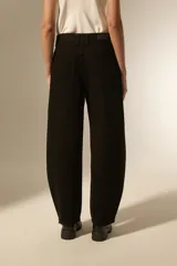 Pantalón de jean negro de corte ancho y tiro bajo, con detalles de tachas metálicas en los bolsillos delanteros y a lo largo de las costuras laterales.