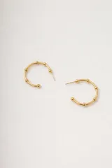 Par de aros tipo argolla abierta de metal dorado, con pequeñas esferas decorativas a lo largo del cuerpo del aro.