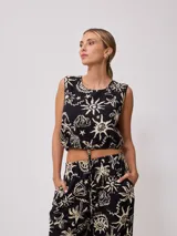 Top corto negro con estampado de flores y figuras geométricas en color crema, con breteles anchos y lazo ajustable en la cintura.