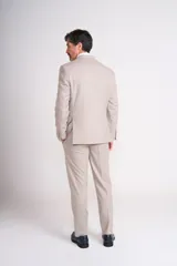 Traje de vestir color beige, compuesto por saco de dos botones con solapa de muesca, bolsillo de ojal en el pecho y bolsillos con solapa en los laterales, y pantalón de vestir de corte recto. Incluye pañuelo de bolsillo azul con lunares blancos.