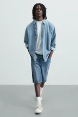 Bermuda de denim de algodón, color gris claro lavado, de corte ancho (baggy fit) y largo hasta la rodilla. Presenta cinco bolsillos y cierre frontal con cremallera y botón.