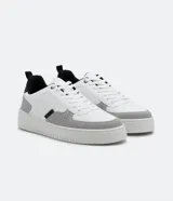 Championes urbanos de cuero sintético blanco con recortes en gris y negro, cierre con cordones y suela de goma.