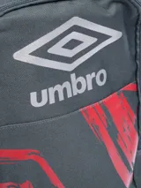 Mochila Umbro modelo Bloop, color gris oscuro con estampado frontal en rojo y detalles en rojo en las cremalleras. Posee bolsillo lateral de malla para botella y logo Umbro plateado en la parte superior.